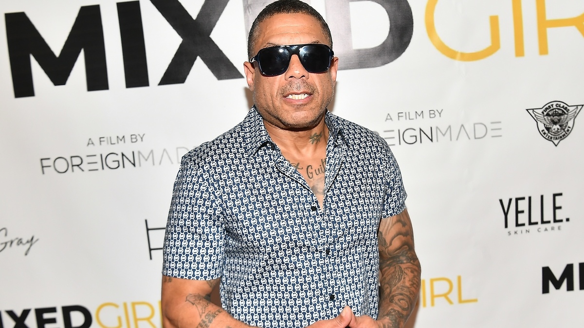 Man in patterned short-sleeved shirt and sunglasses posing at event with 'MIXED GIRL' backdrop