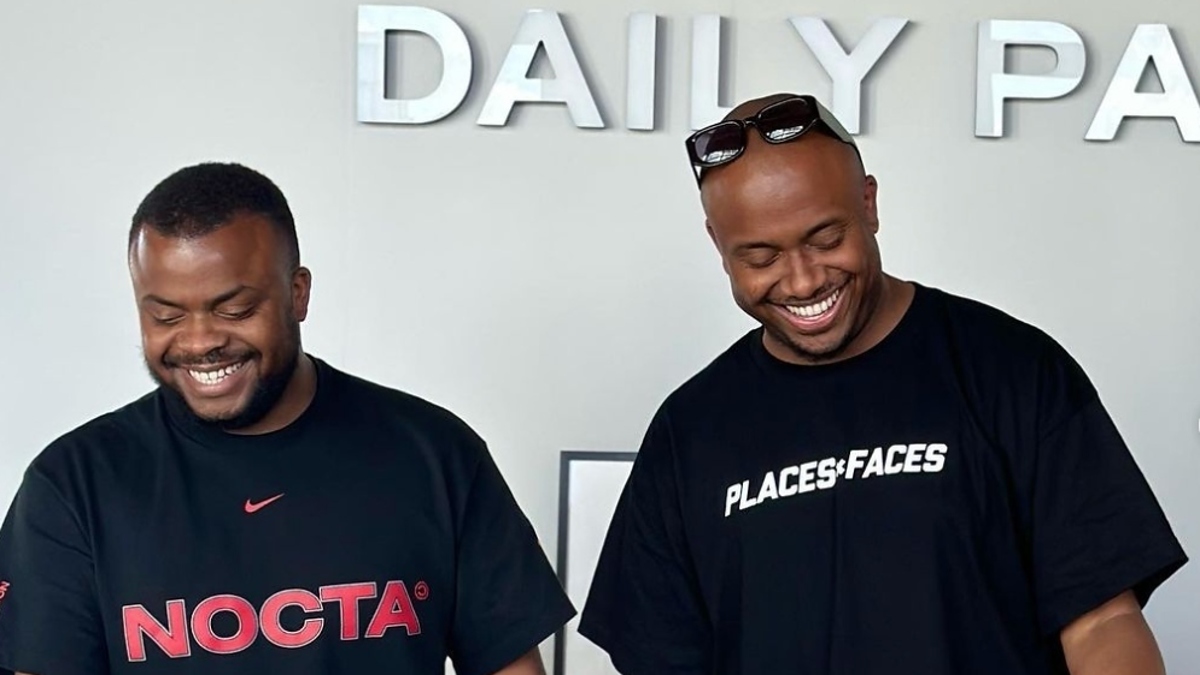 Two individuals standing, wearing branded t-shirts, smiling at an unseen object on a counter