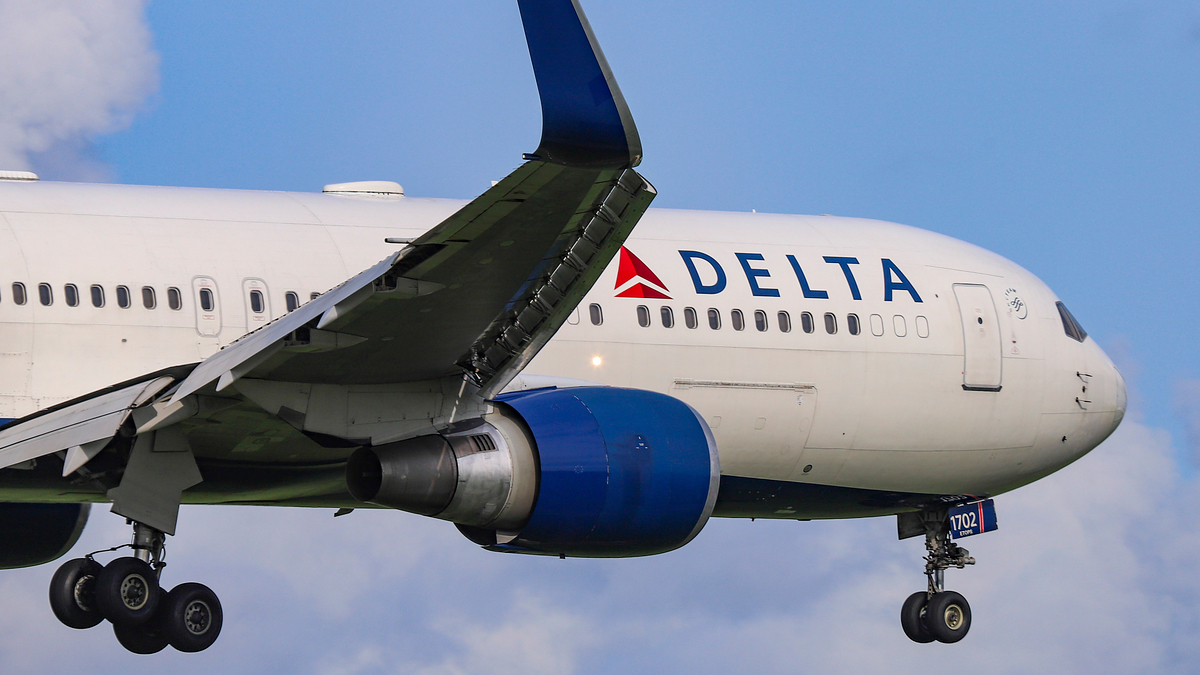 Delta Airlines aircraft mid-flight with landing gear down against a blue sky