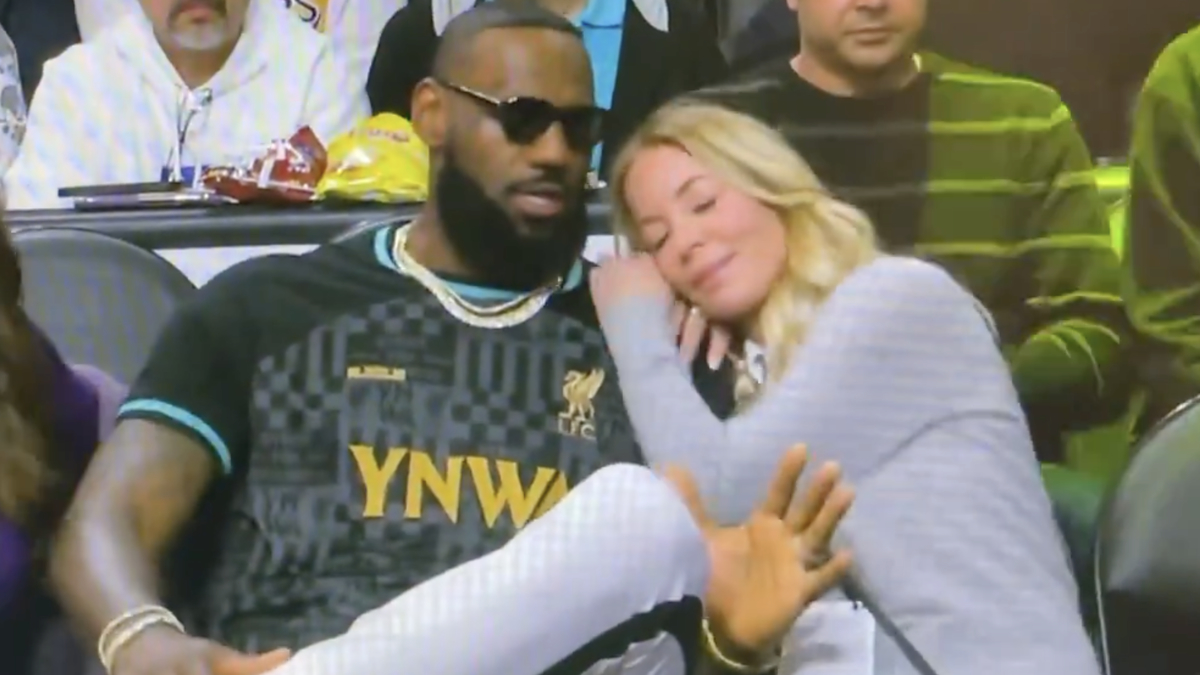 LeBron James in a black jersey seated courtside next to a woman in a grey top