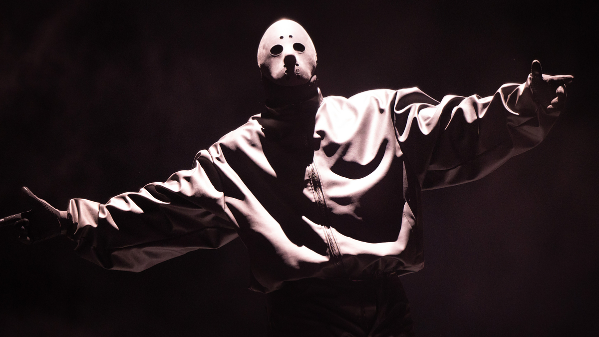 Performers in masks and dark attire pose on stage