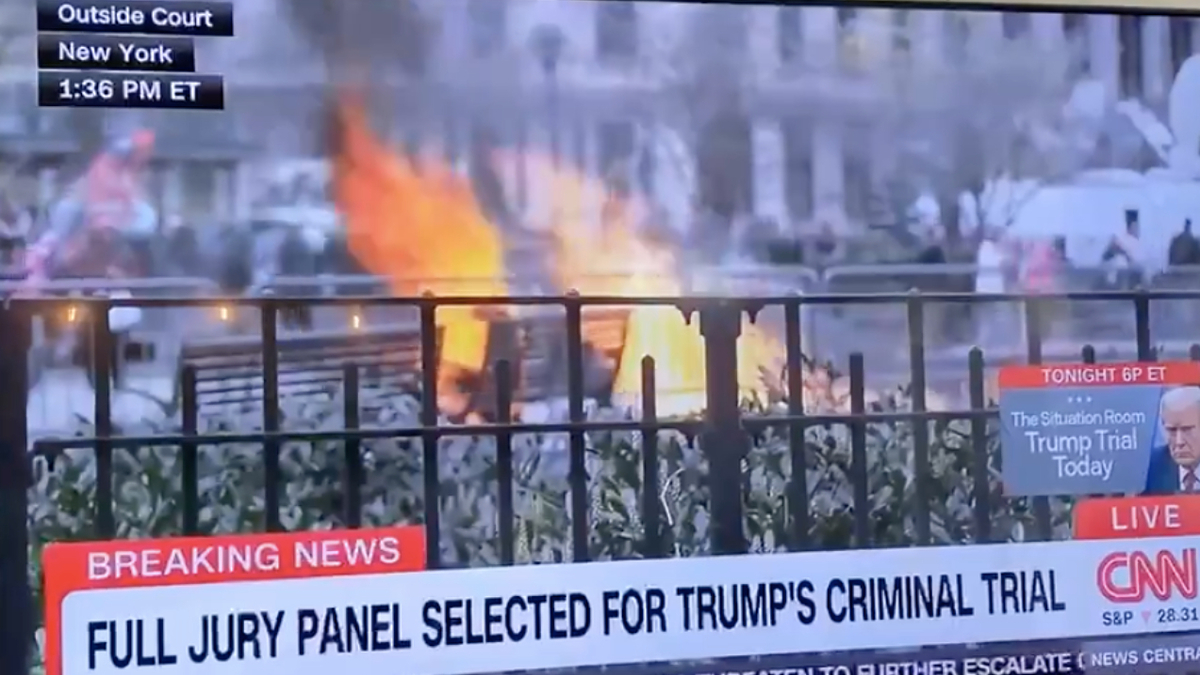 A TV screen showing a CNN Breaking News about the selection of a jury panel with a visible fire in the background