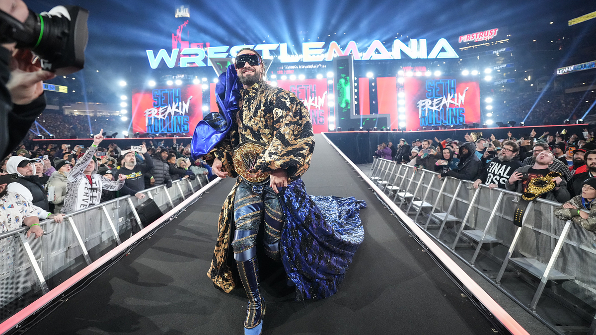 Wrestler in ornate robe with championship belt walks down ramp at WrestleMania event