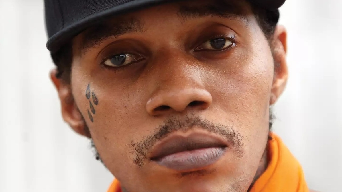 Close-up of a musician in a hat, with a facial tattoo on the left cheek