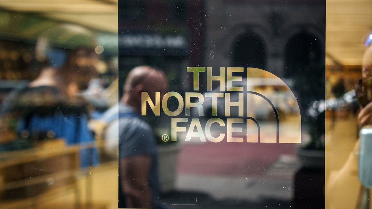 The North Face logo on a glass window with blurred figures and store interior visible in the background