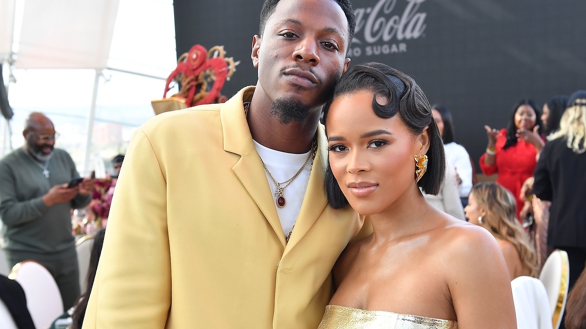 Two individuals posing, one in a yellow blazer, the other in a strapless dress, at an event