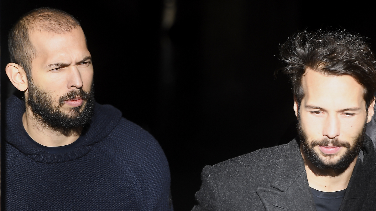 Two men walking side by side, one in a dark sweater, the other in a grey coat