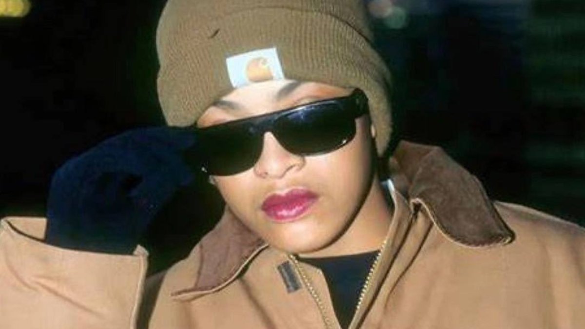 Person in beanie and sunglasses with coat and glove, looking away from camera