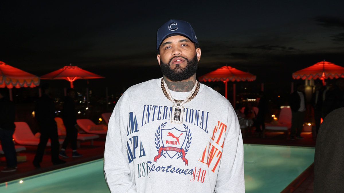 Man in branded sweatshirt and cap standing by a pool at an evening event