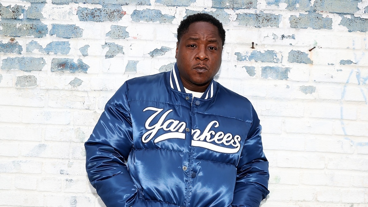 Man standing against a brick wall wearing a Yankees bomber jacket and red shorts