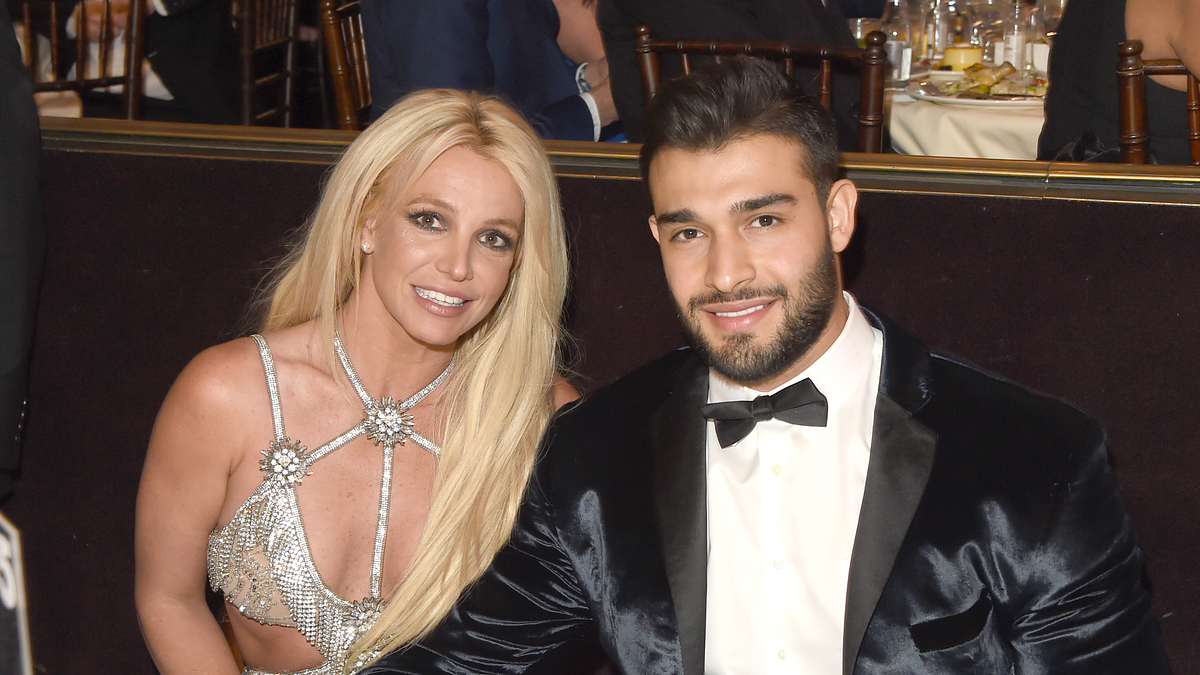 Britney Spears in a sparkling dress and Sam Asghari in a tuxedo sitting at a dinner table