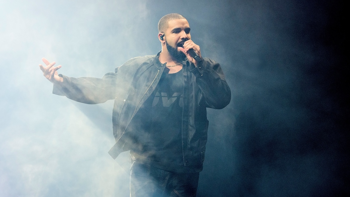 Drake performing on stage, holding a microphone, with stage smoke around him