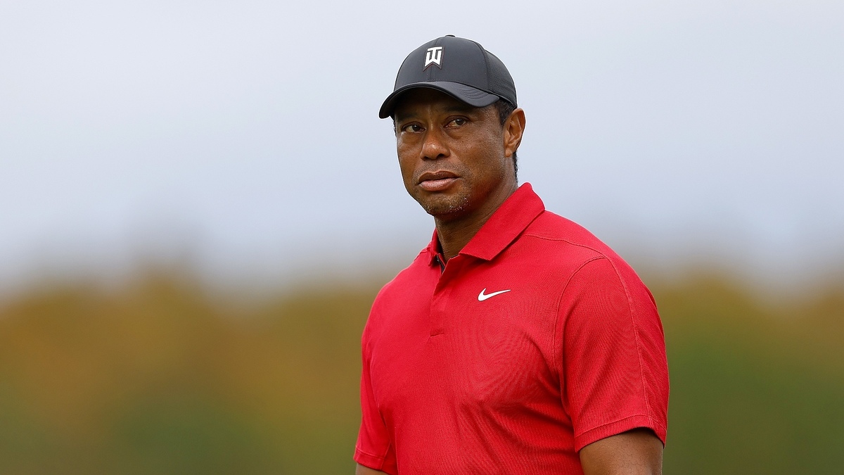 Tiger Woods wearing a red shirt and cap, staring into the distance on a golf course
