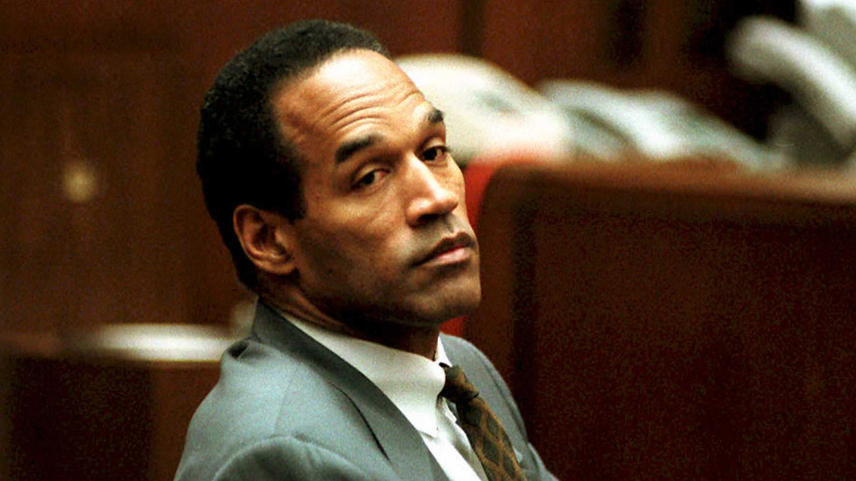 Man in a courtroom wearing a suit and tie, looking over his shoulder