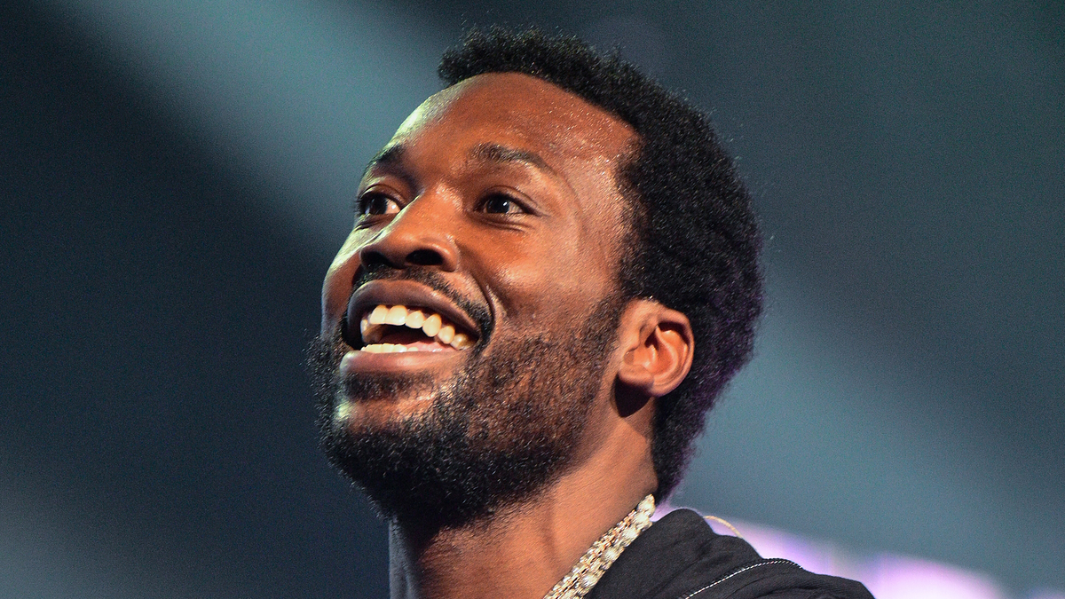 Man smiling on stage wearing a hoodie and a chain necklace