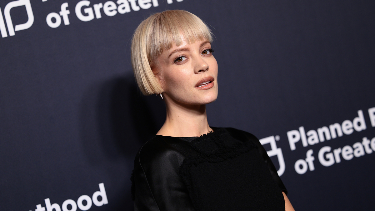 Lily Allen in black outfit on event backdrop, looking at camera, short hair styled