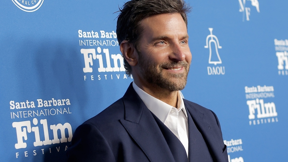 Man in dark suit smiles at an event with logos in the background