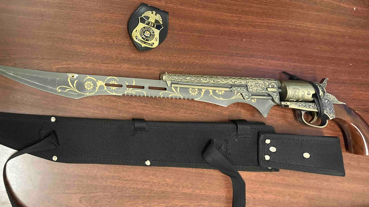 Decorative revolver with ornate engravings next to a matching knife on a desk near a law enforcement badge