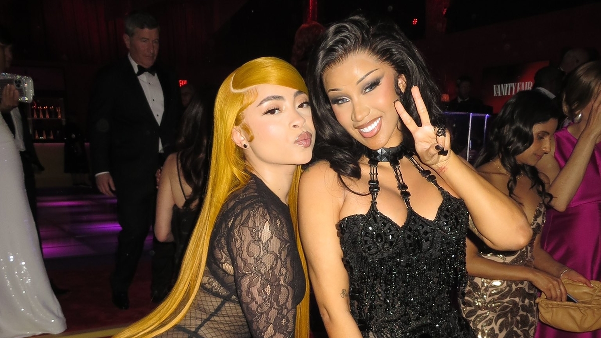 Two women posing at an event, one in a sheer gown with bodysuit, the other in a beaded black dress