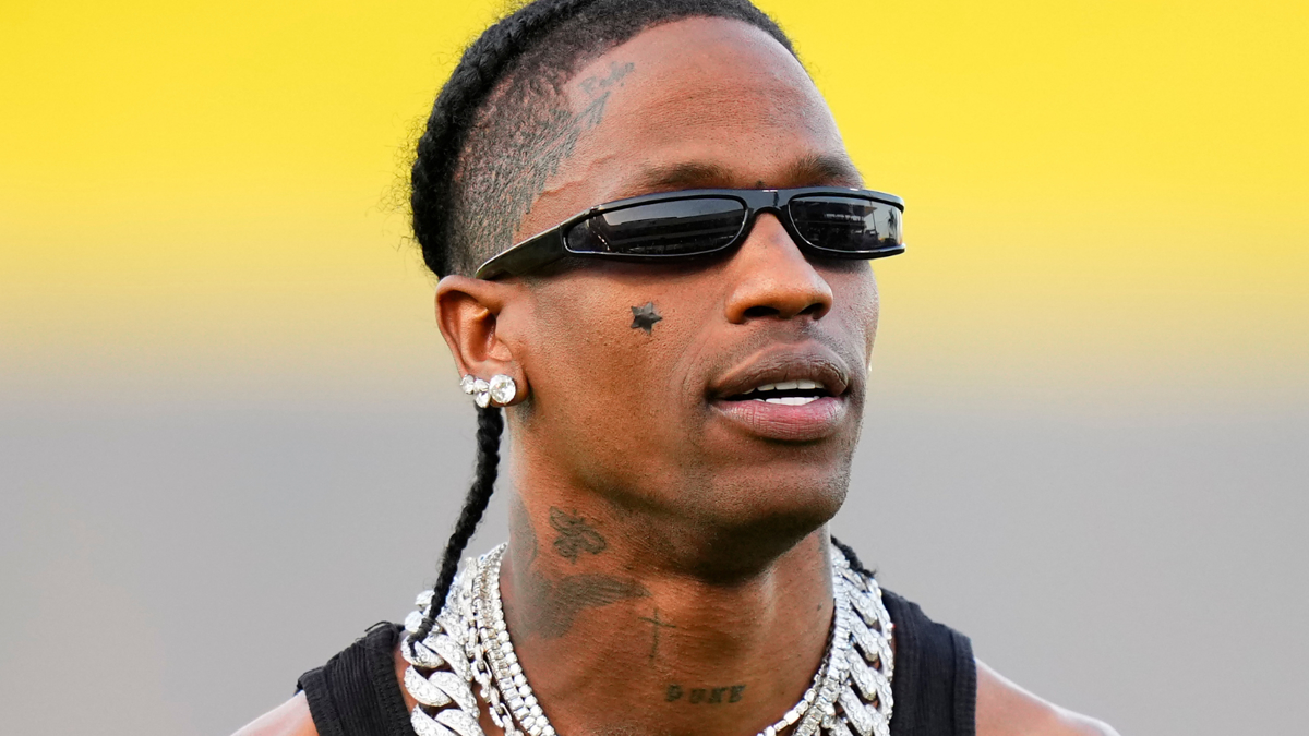 Travis Scott wearing sunglasses, chains, and a sleeveless top