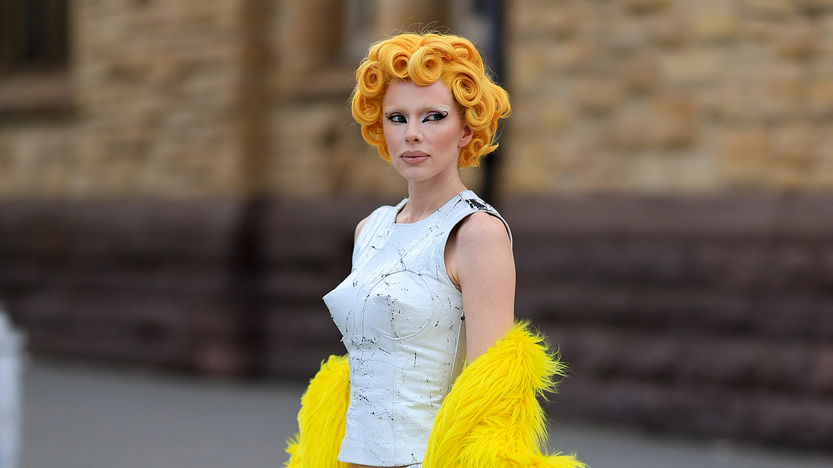 Woman in avant-garde white dress with yellow feather details, sporting sculptural orange hair