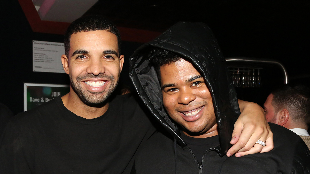 Two men smiling with their arms around each other, one wearing a black hoodie