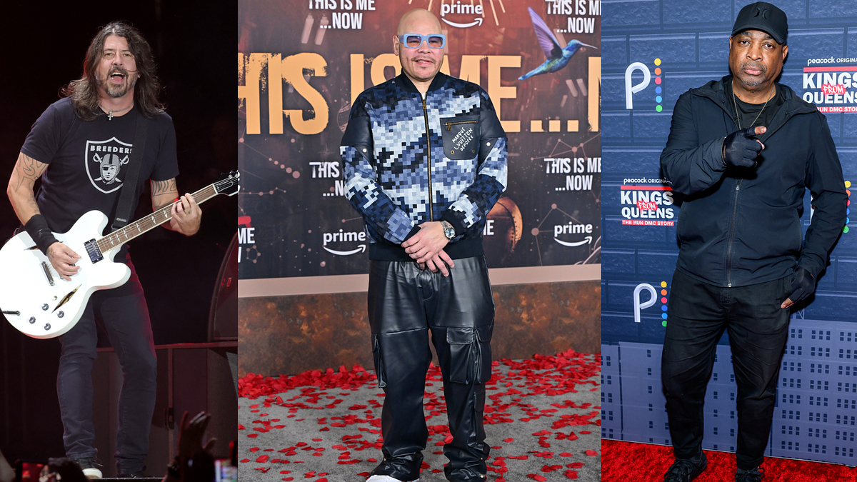 Guitarist performing; two men on red carpet, one in patterned suit, one in casual attire