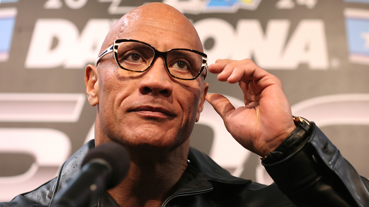 Rock in formal attire adjusting glasses at a press event