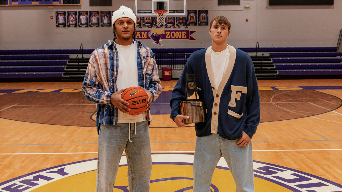 Two individuals standing on a basketball court, one holding a basketball, both wearing casual attire with prominent lettering