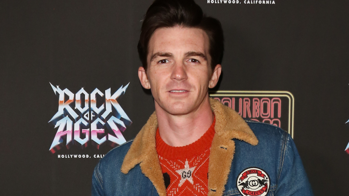 Man in denim jacket and red sweater posing at 'Rock of Ages' event