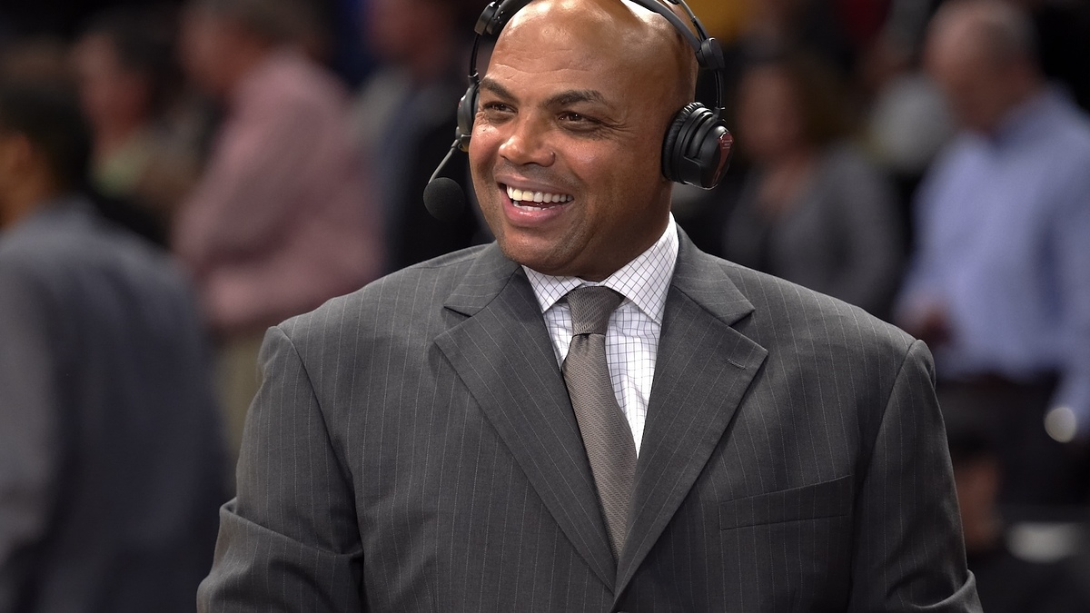 Smiling man in suit with headphones commentating at a sports event