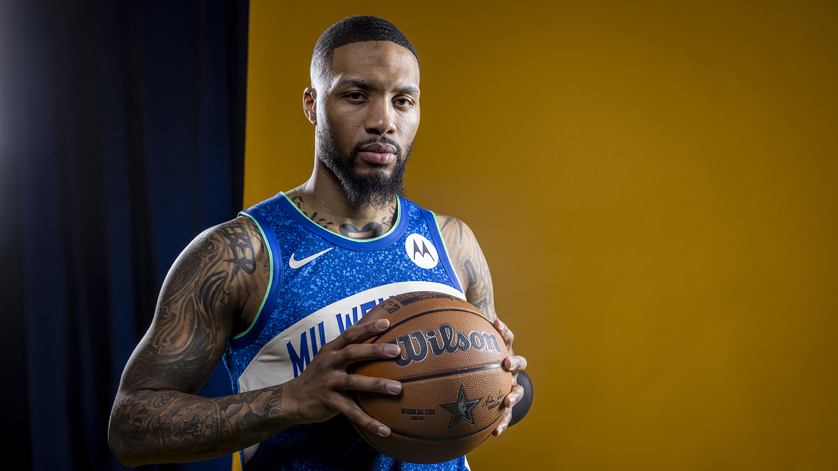 Basketball player in a blue jersey holding a ball, standing against a yellow backdrop