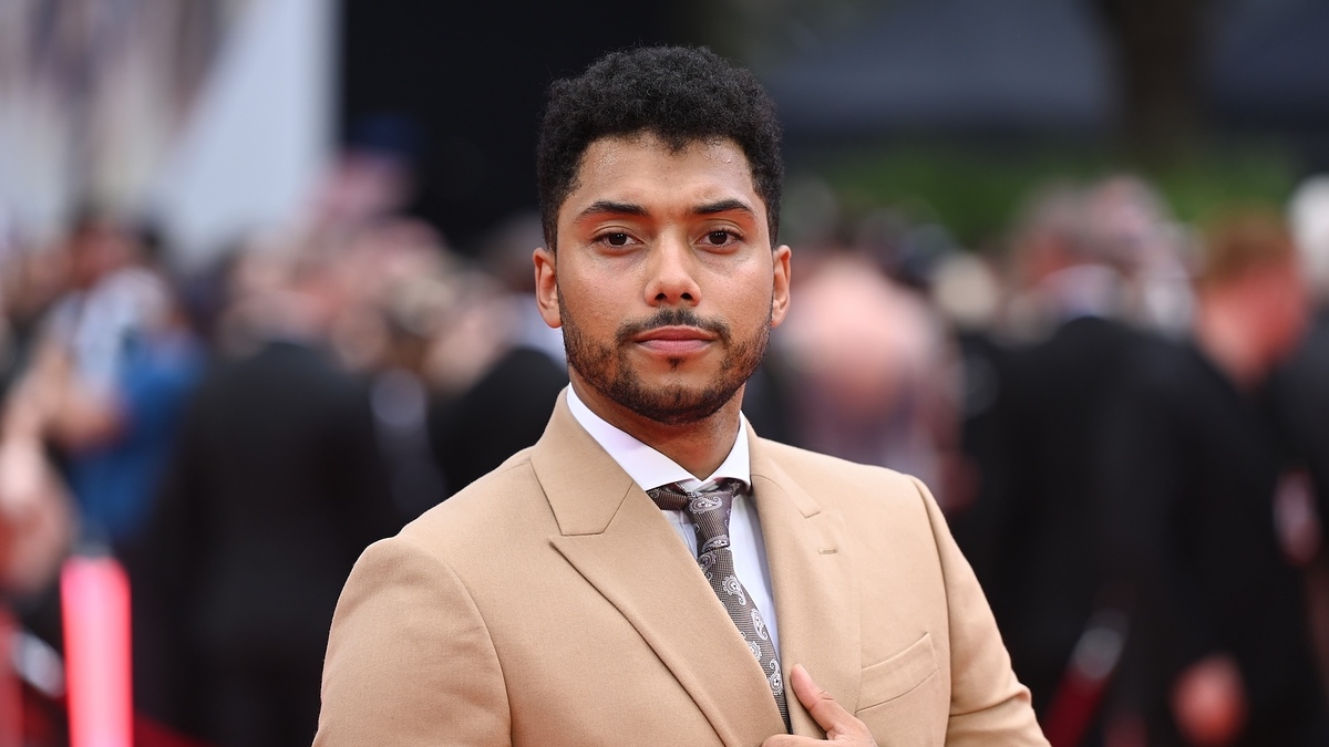 Man in a beige suit with a patterned tie at a red carpet event