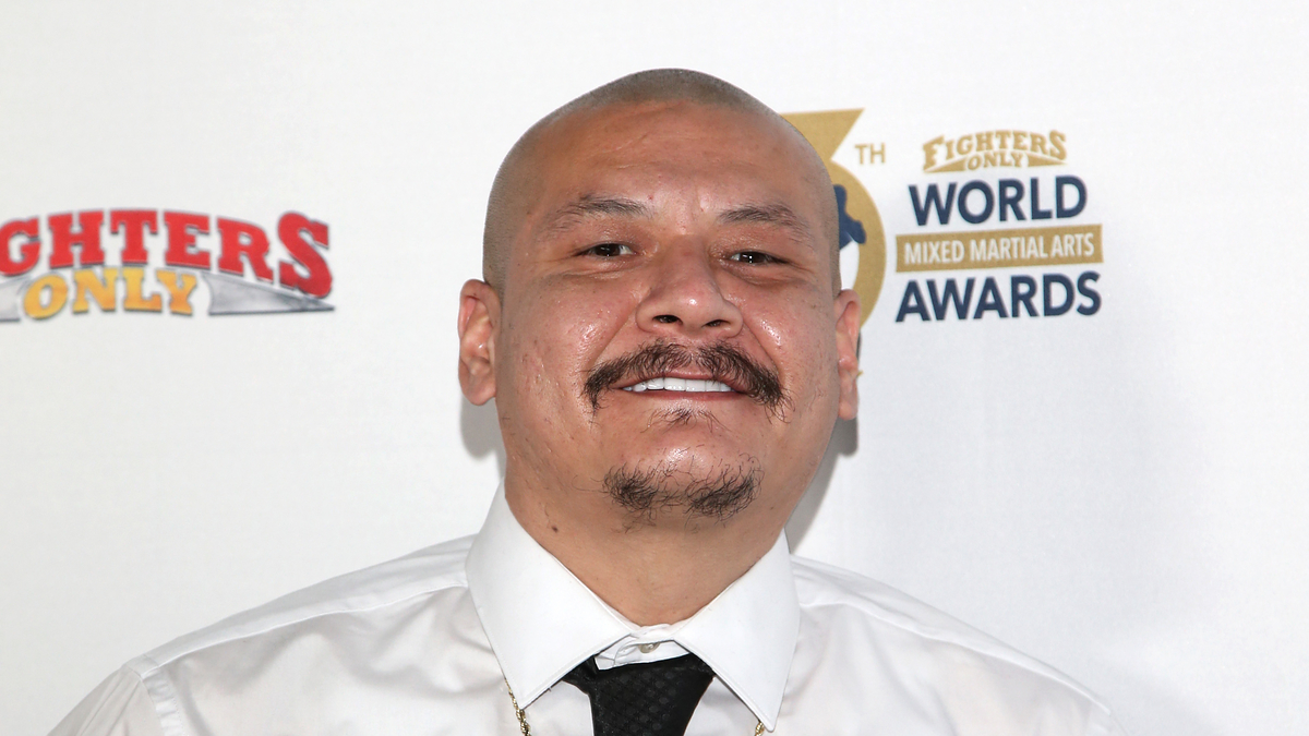 Man in white shirt and tie with a necklace, smiling at an event