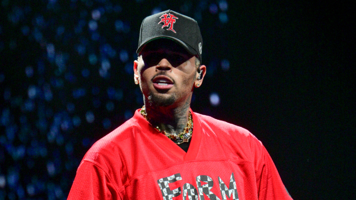 Chris Brown on stage wearing a cap and a red top with a logo