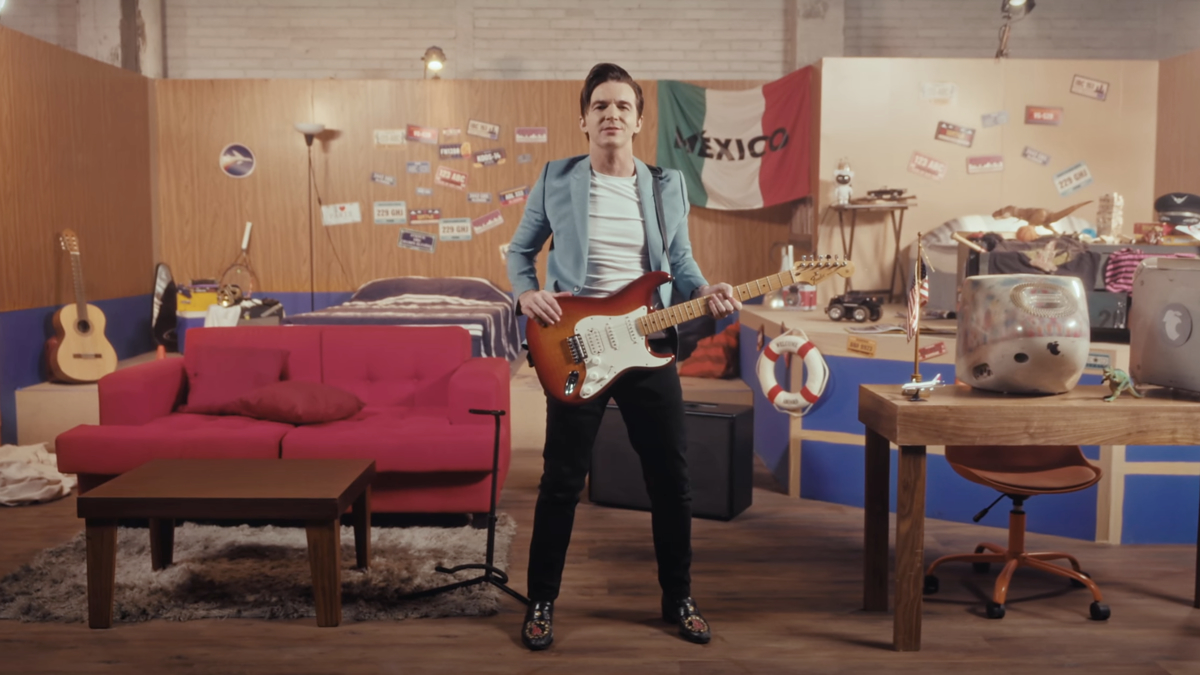 Man stands with guitar in room with various vintage items and flags