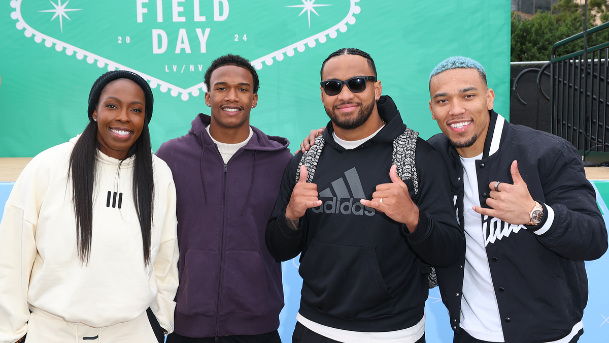 Four athletes posing with thumbs up at a sports event, sporting casual attire and smiles
