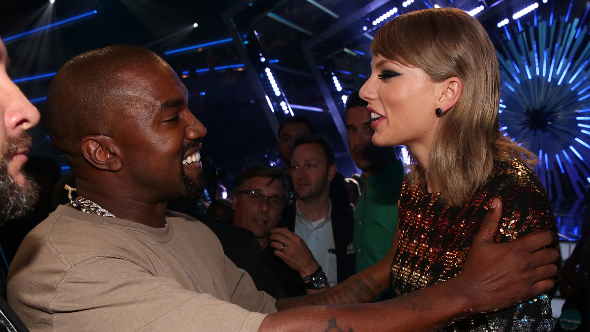 Two celebrities embracing and smiling at an event. The person on the left is wearing a casual outfit, and the person on the right is in a sequined dress