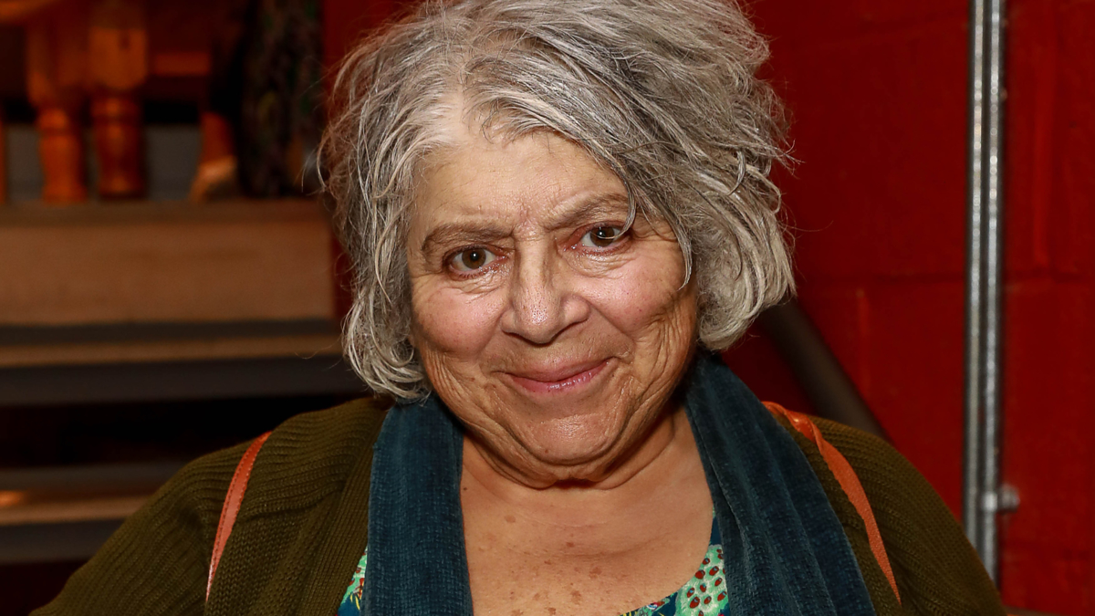 Older woman smiling at the camera with grey hair and wearing a cardigan over a patterned top