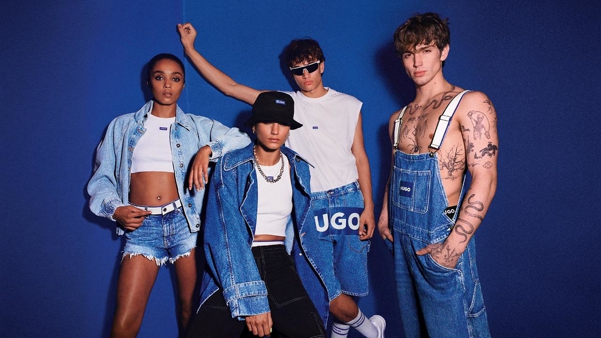 Four models in denim wear pose against a blue backdrop, one with a bucket hat