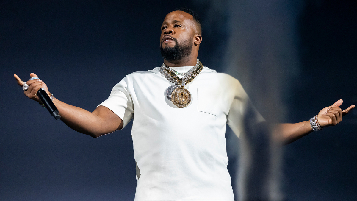 Musician on stage performing, wearing a white t-shirt and gold chain necklace