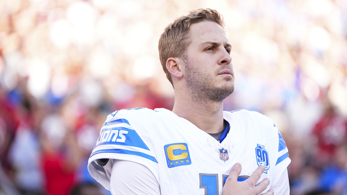 Football player in uniform with captain's "C" patch stands solemnly on the field during a game