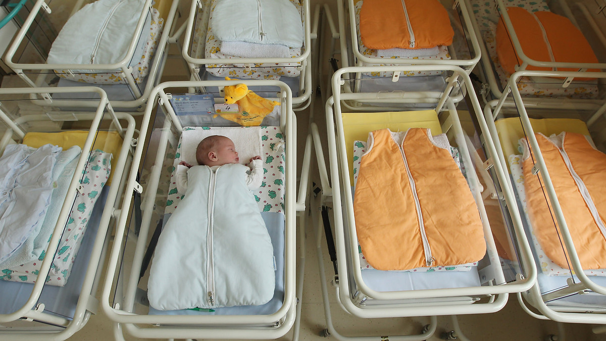 A newborn baby lies in a baby bed in the maternity ward of a hospital.