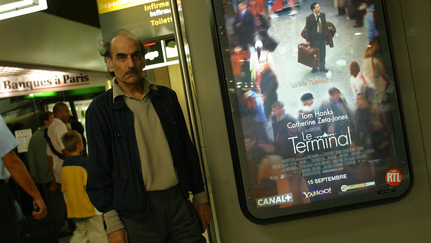 Mehran Karimi Nasseri pictured next to a poster of The Terminal, the movie that he inspired.