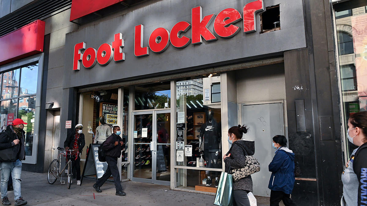 People wearing protective masks walk past a Foot Locker store