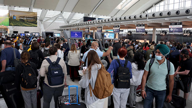 Travelers wearing face masks wait to check-in at Toronto Pearson International Airport on June 30, 2022