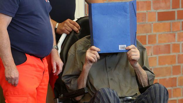 Former Nazi concentration camp guard Josef Schuetz (R) covers his face as he arrives on June 28, 2022 at a gym used as a makeshift courtroom