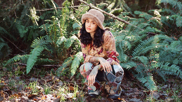 Kehlani crouching in a wooded area.