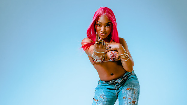 Tia Bank$ pointing at the camera, wearing a bikini top and ripped blue jeans