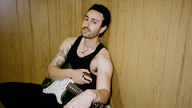 Jesse Gold sitting behind wood panelling holding a Stratocaster